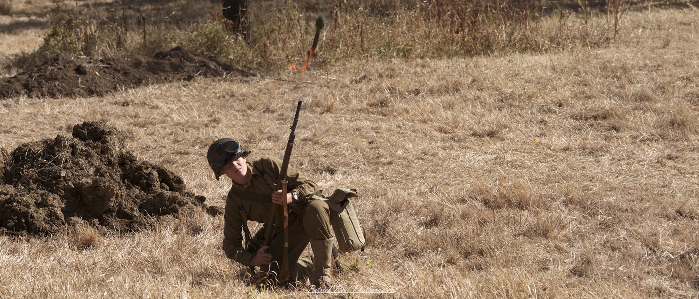 "Image of a soldier firing a rifle grenade from an M1 Garand during World War II. The soldier is positioned in a combat-ready stance, with the rifle held at shoulder level, as the grenade is launched from the barrel. The scene captures the intensity of battle, with dirt and debris flying around him. The soldier's uniform is typical of the era, featuring a helmet and gear appropriate for the time. The background depicts a war-torn landscape, emphasizing the action and urgency of the moment."